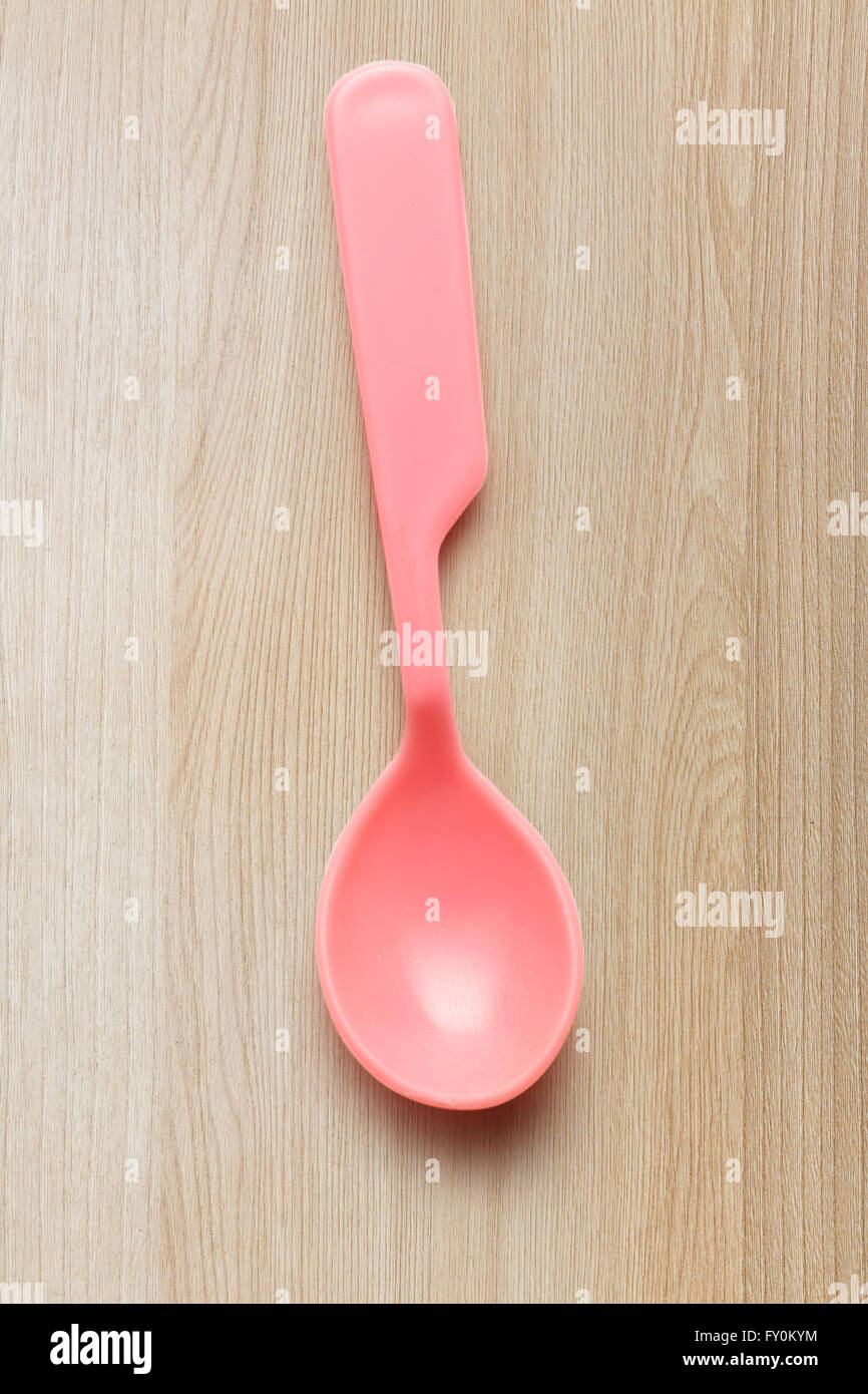 Rosa di stoviglie di plastica cucchiaio su sfondo di legno Foto Stock