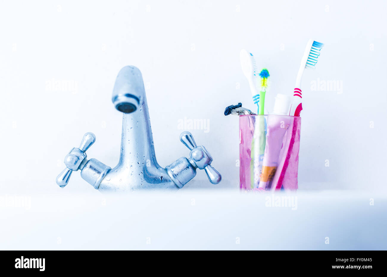 Bicchiere di plastica con gli spazzolini da denti sul bacino vicino al rubinetto di acqua Foto Stock