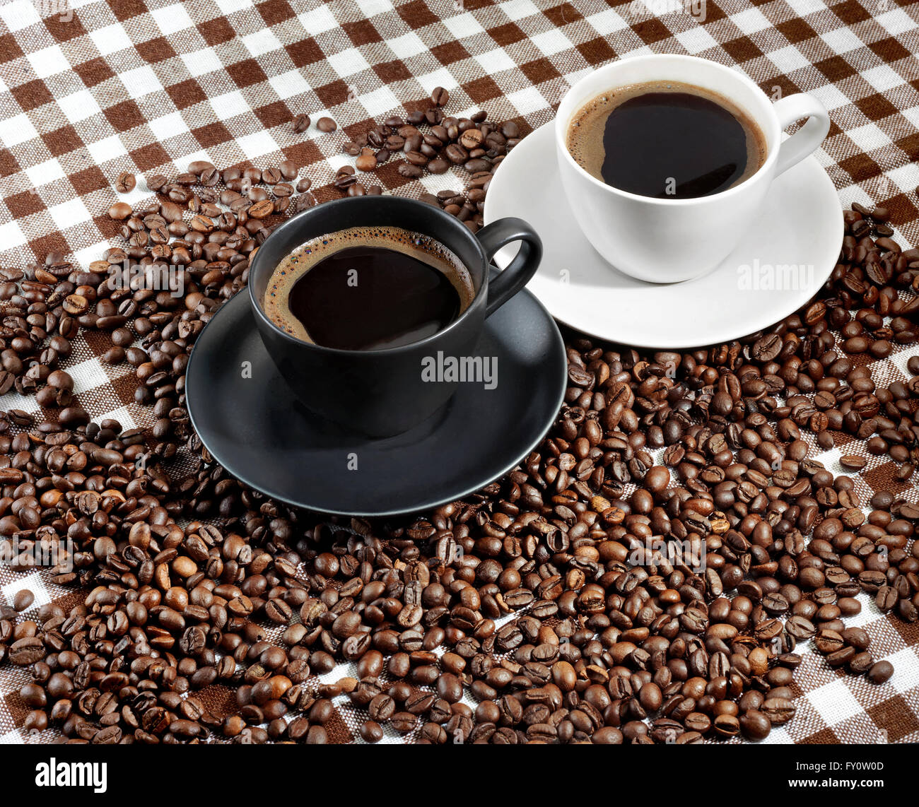 Due tazze di caffè e caffè in grani su un panno a scacchi Foto Stock