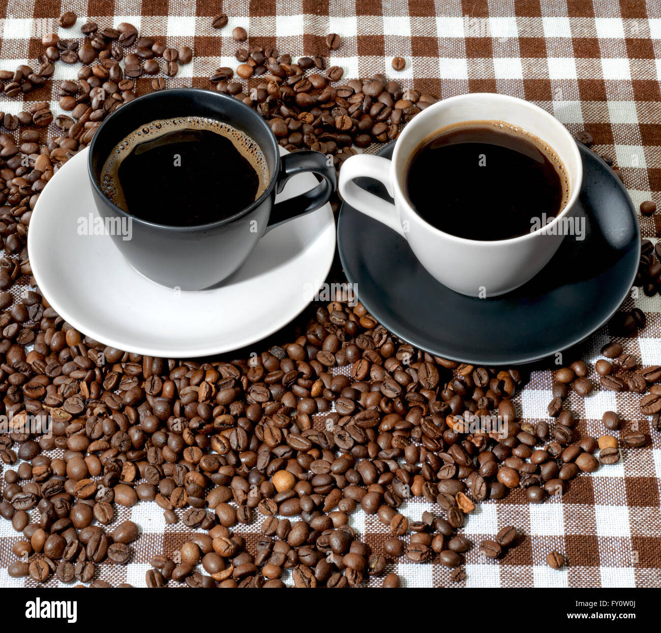 Due tazze di caffè e caffè in grani su un panno a scacchi Foto Stock
