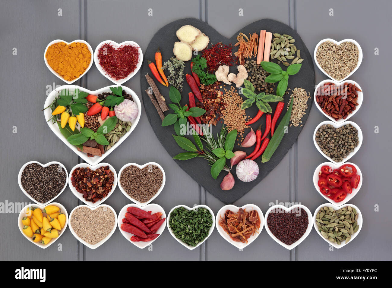 Erbe e spezie ingredienti su una a forma di cuore e di ardesia in piatti di porcellana di legno su sfondo grigio. Foto Stock