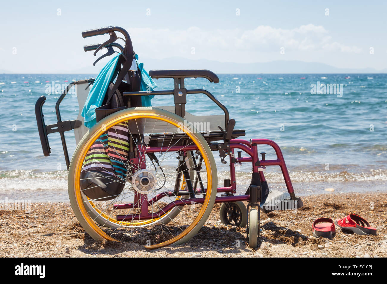 Sedia a rotelle sulla spiaggia contro il blu del mare in estate Foto Stock