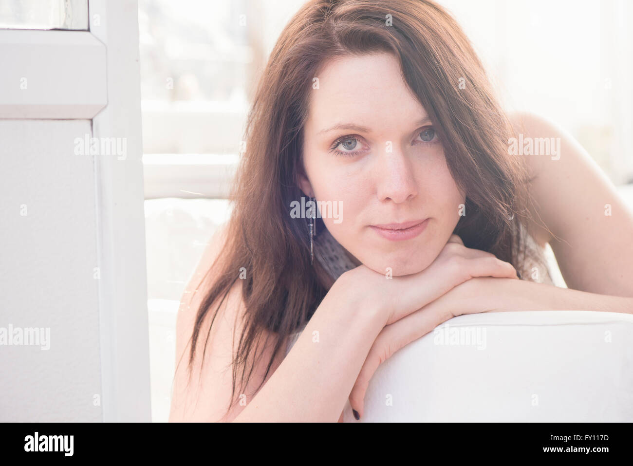 Ritratto di giovane donna sdraiata sul divano. Guarda la fotocamera con un grave e espressione annoiata. Foto Stock