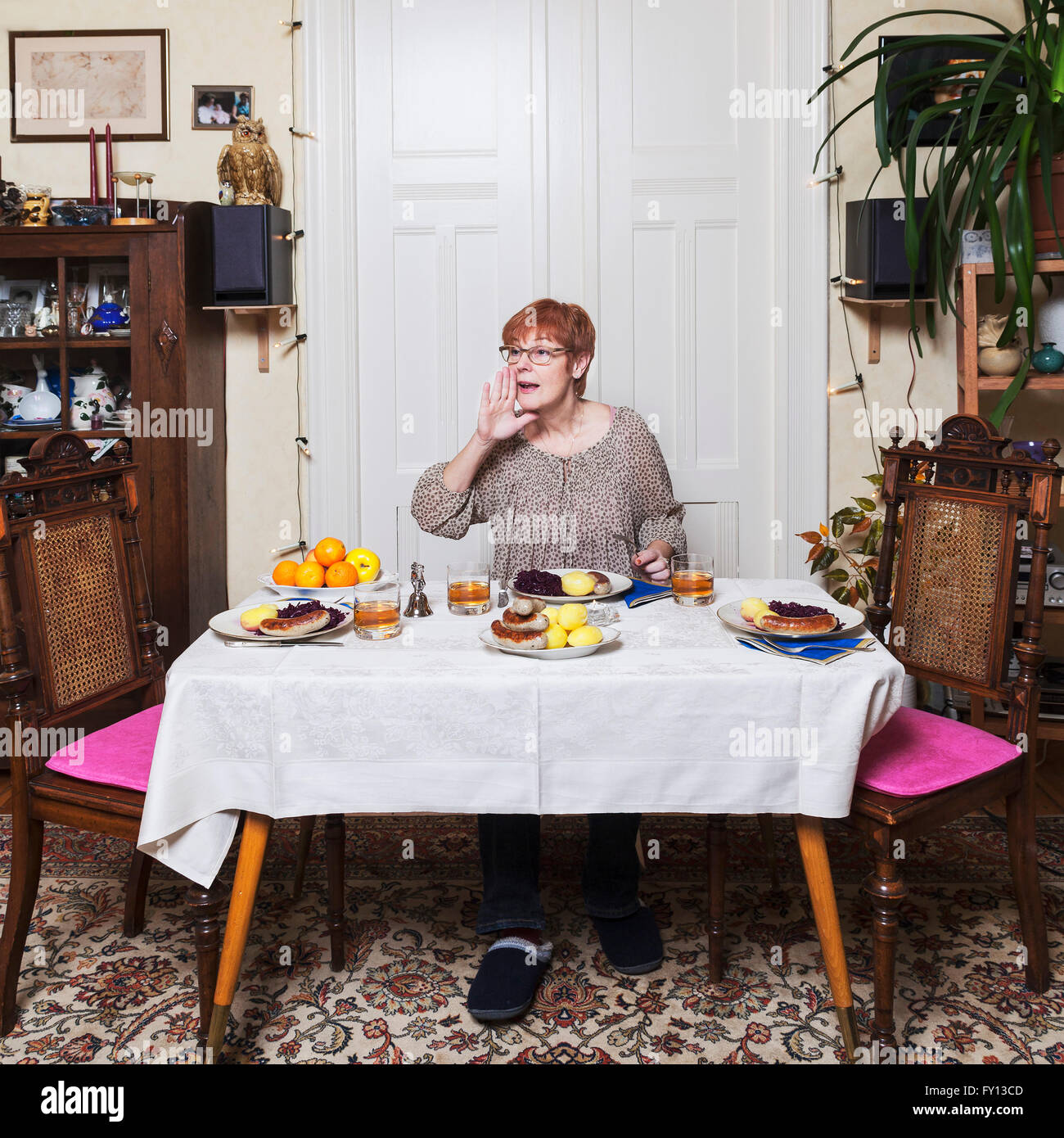Donna matura coppettazione la mano alla bocca mentre avente il cibo in tavola Foto Stock