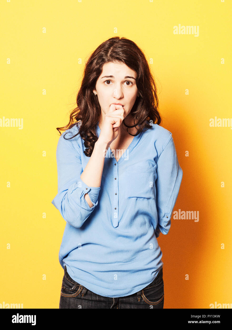 Ritratto di giovane nervoso donna mordere le unghie contro sfondo giallo Foto Stock