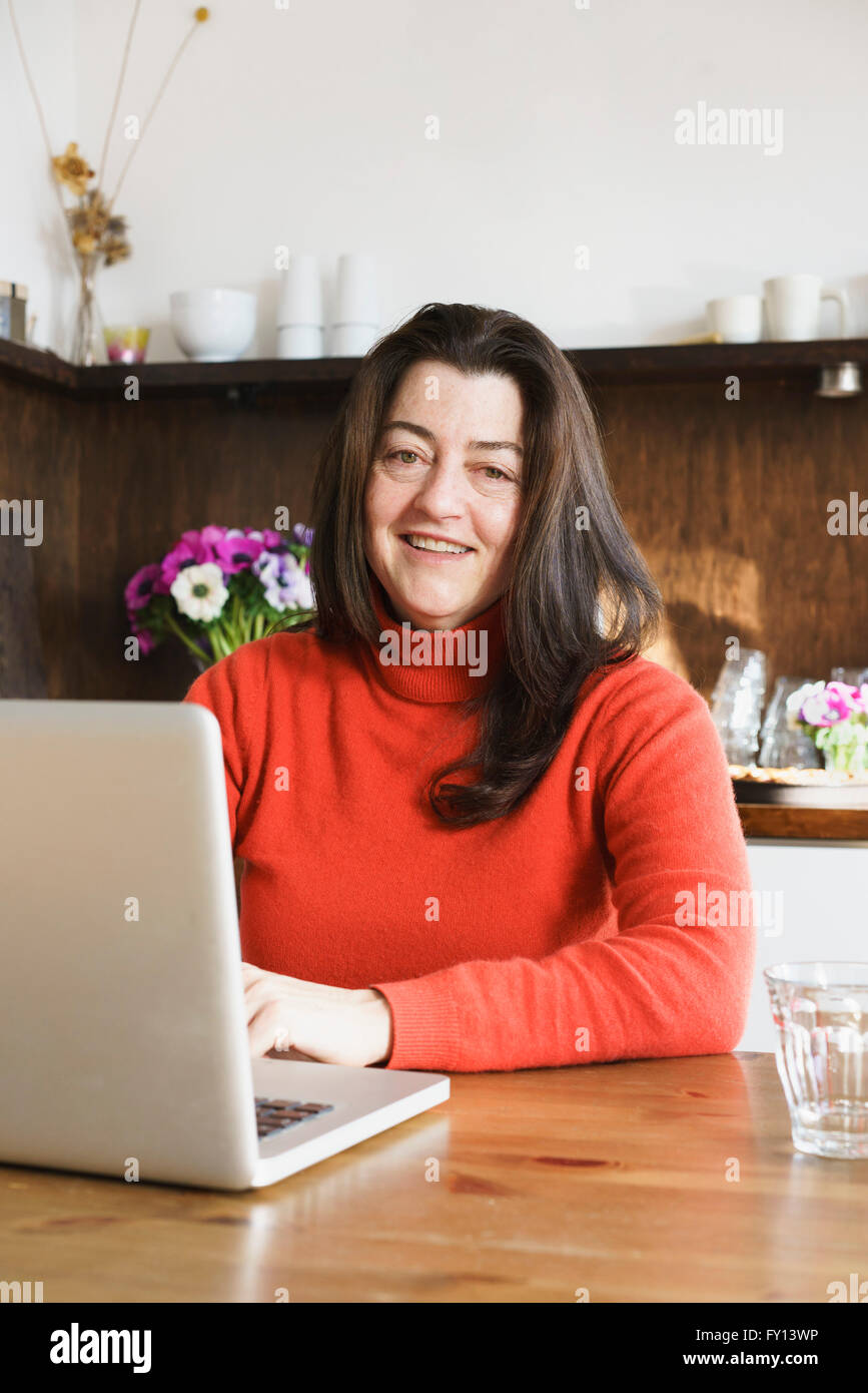 Ritratto di sorridere donna matura utilizzando portatile a casa Foto Stock
