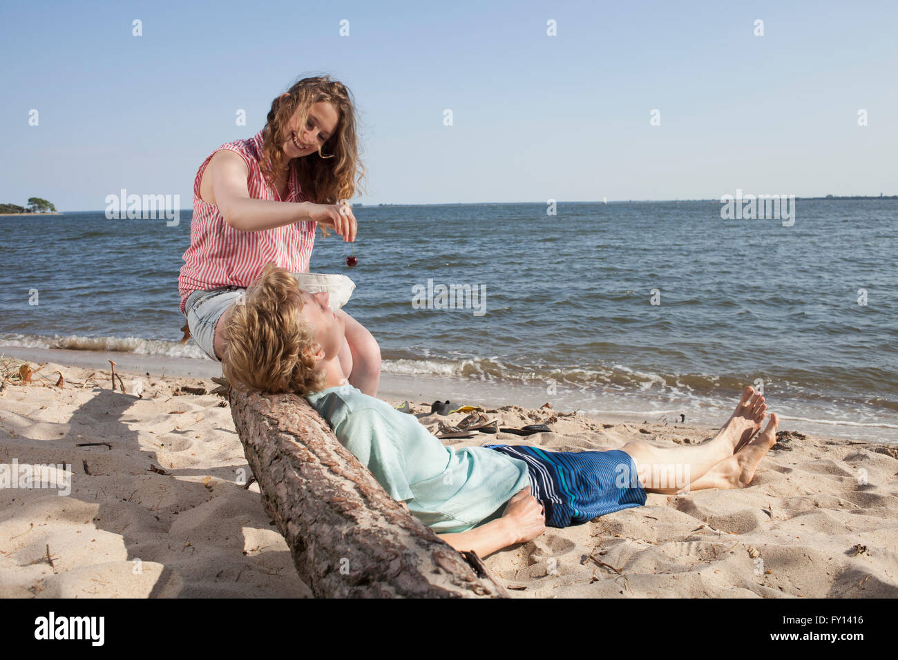 Donna sorridente ciliegia di alimentazione ad un amico durante i momenti di relax in spiaggia Foto Stock
