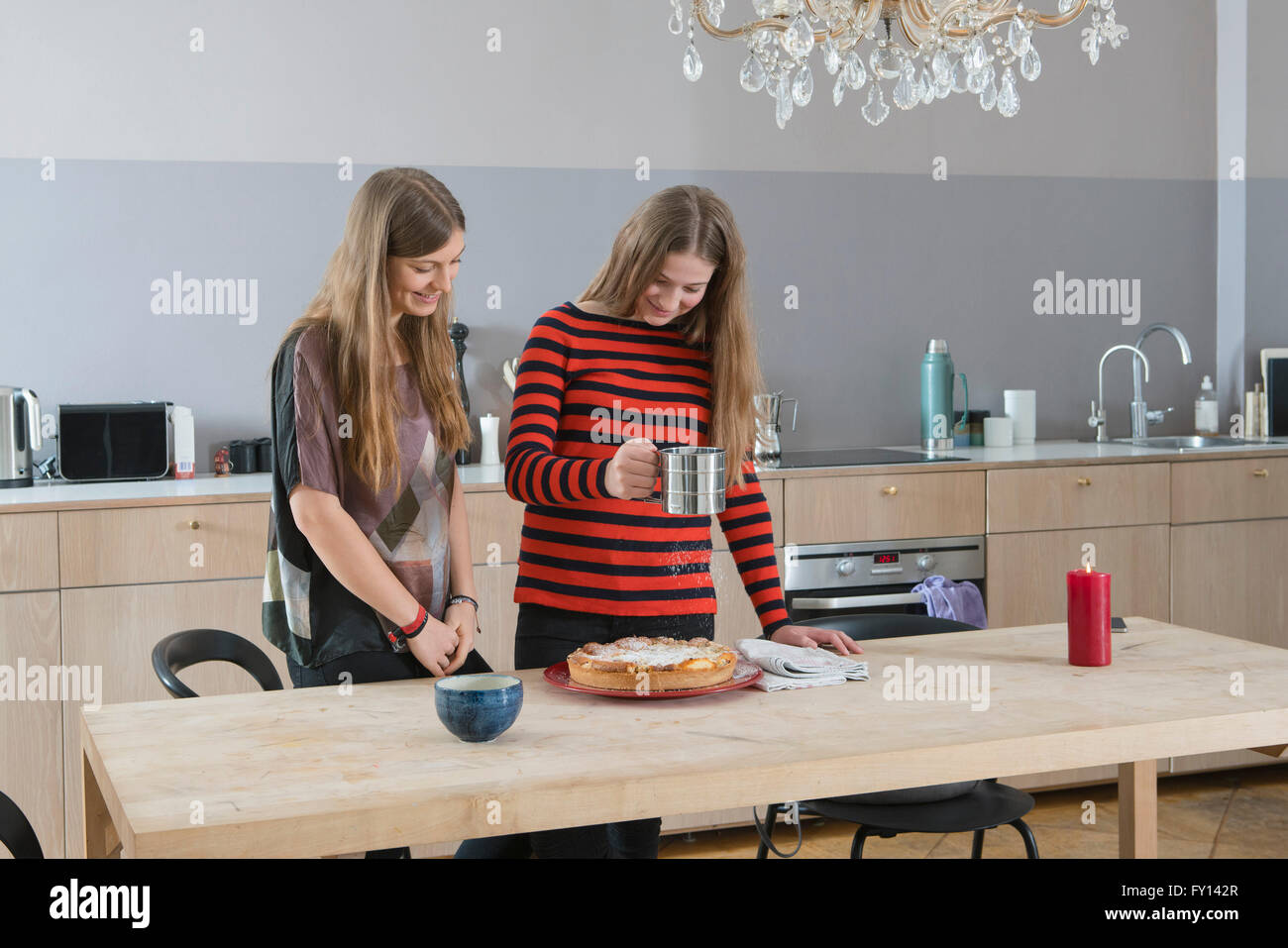 Giovane donna guarda la sorella crostata spolverata con zucchero a velo in cucina Foto Stock