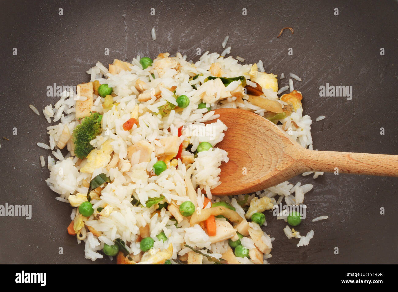 Primo piano del pollo, uova e verdure saltate in padella il riso in un wok con un cucchiaio di legno Foto Stock