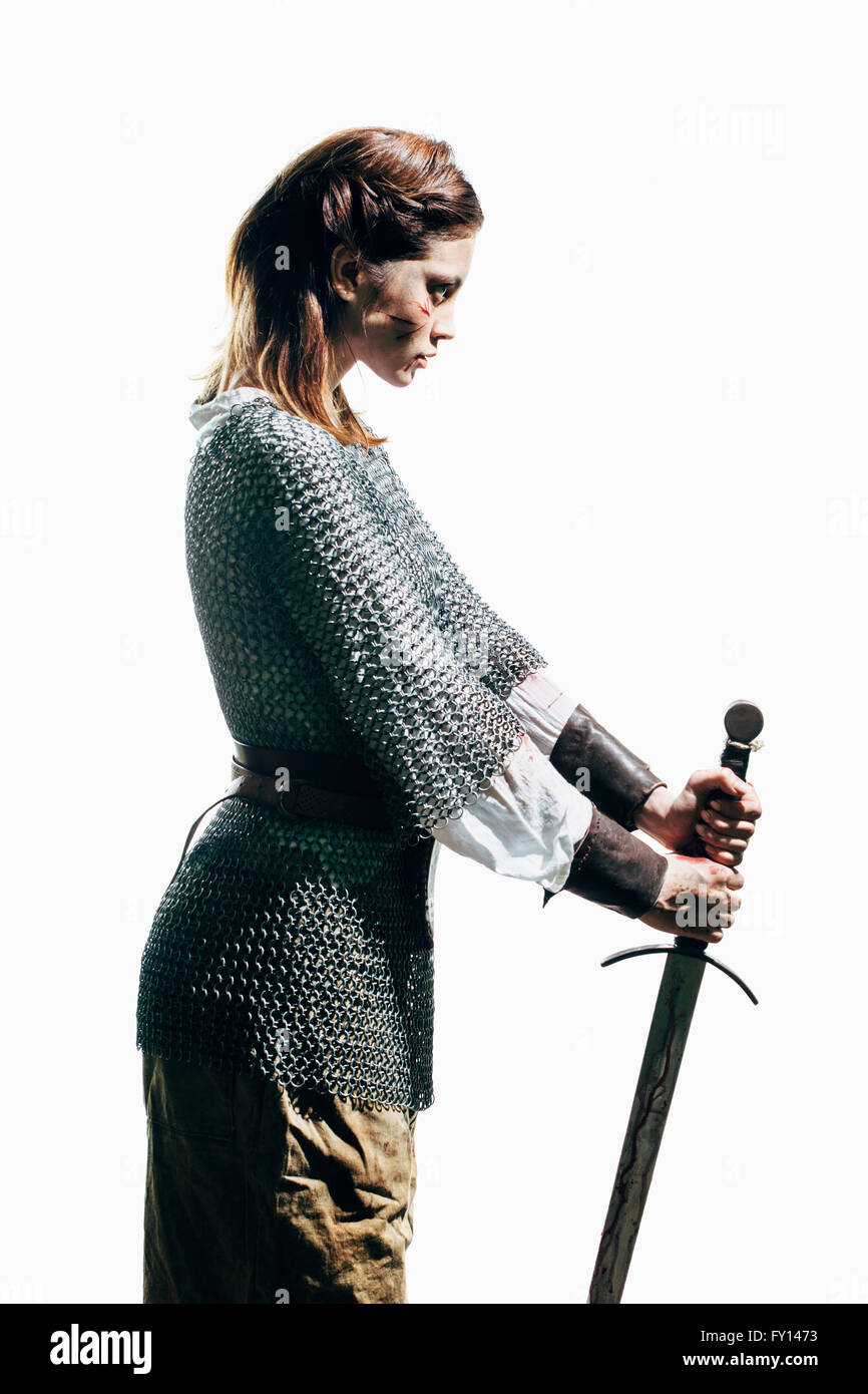 Vista laterale della donna che indossa mail a catena con la spada in piedi contro uno sfondo bianco Foto Stock