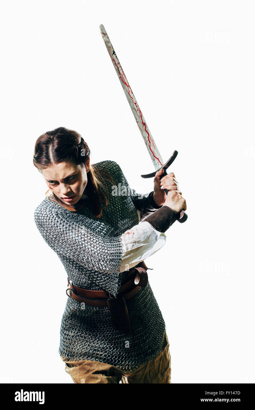 Arrabbiato donna che indossa la catena posta tenendo la spada contro uno sfondo bianco Foto Stock