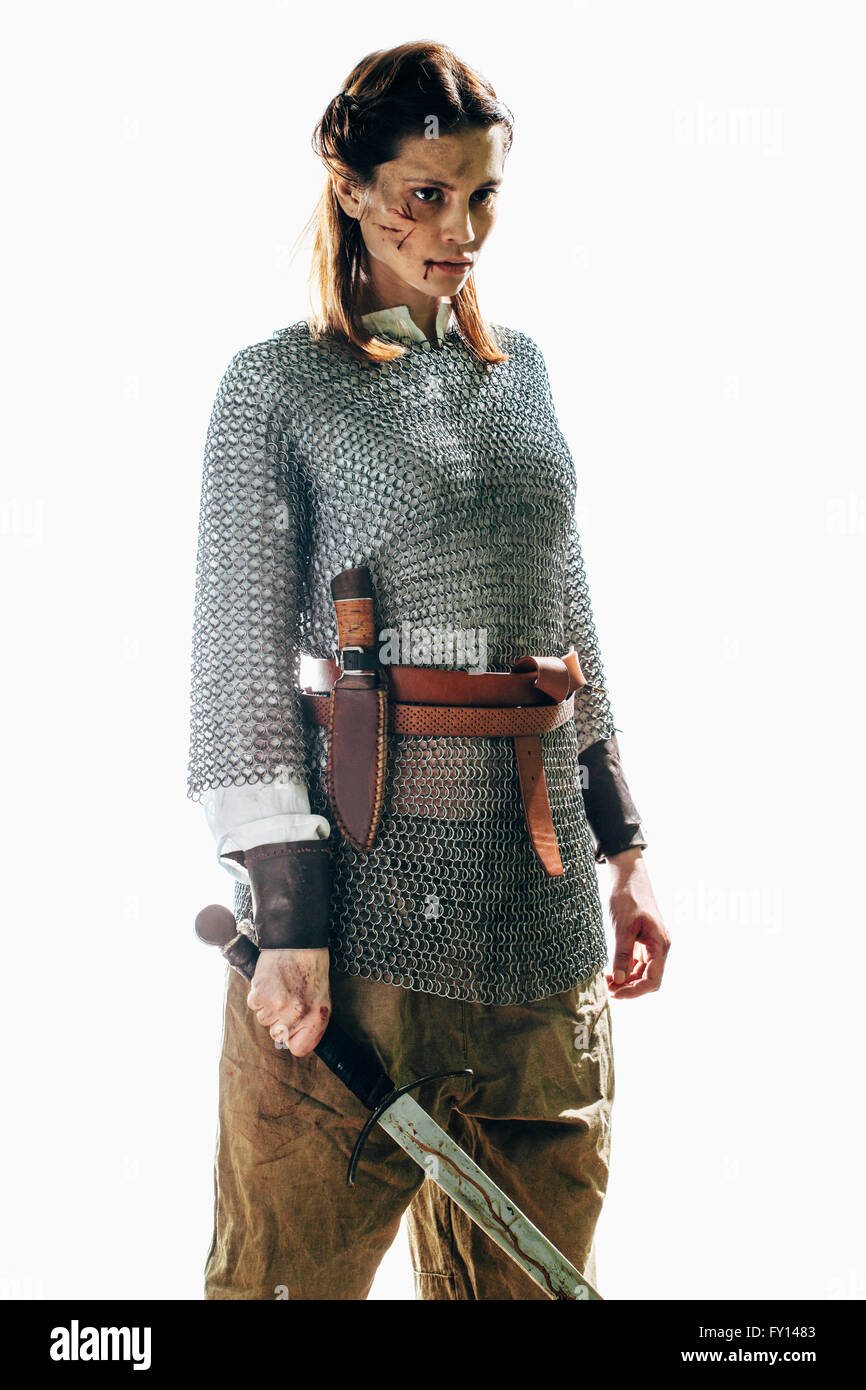 Feriti donna che indossa la catena posta tenendo la spada contro uno sfondo bianco Foto Stock