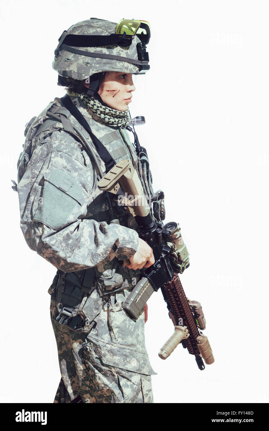 Vista laterale del soldato femmina portando fucile mentre in piedi contro uno sfondo bianco Foto Stock