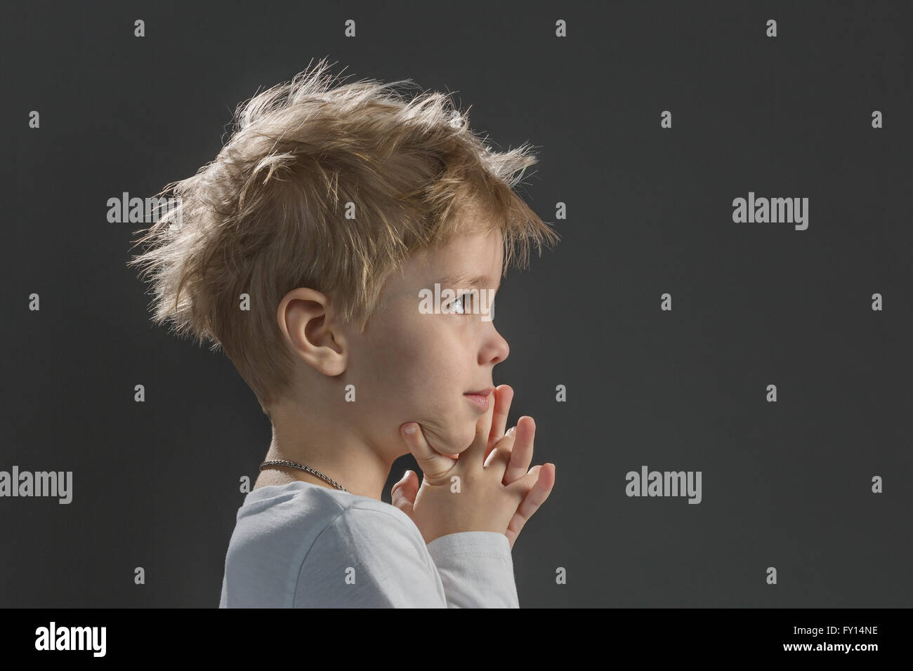 Close-up di pensosa ragazzo con mano sul mento contro lo sfondo grigio Foto Stock