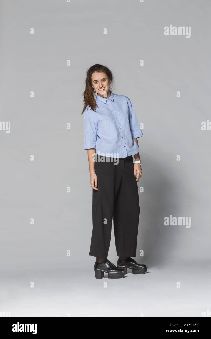 Lunghezza completa donna sorridente in piedi contro lo sfondo grigio Foto Stock
