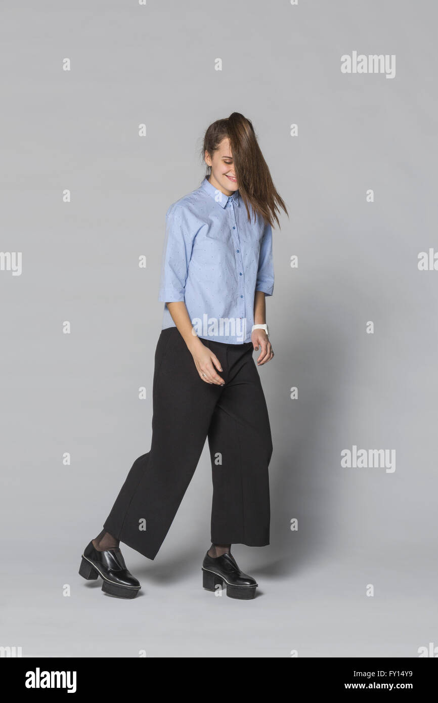 Per tutta la lunghezza della donna sorridente con capelli tousled in piedi contro lo sfondo grigio Foto Stock