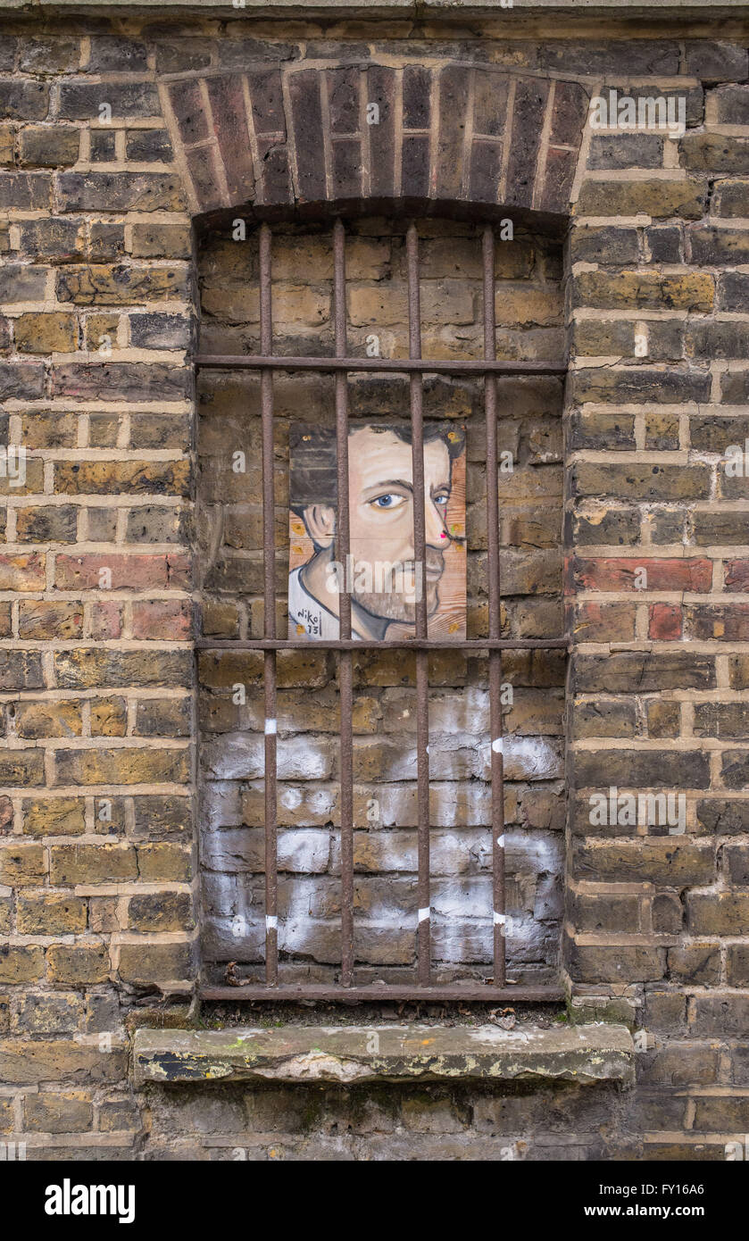 Ritratto di un giovane uomo appeso ad un muro di mattoni dietro le barre metalliche di una vecchia finestra. Foto Stock