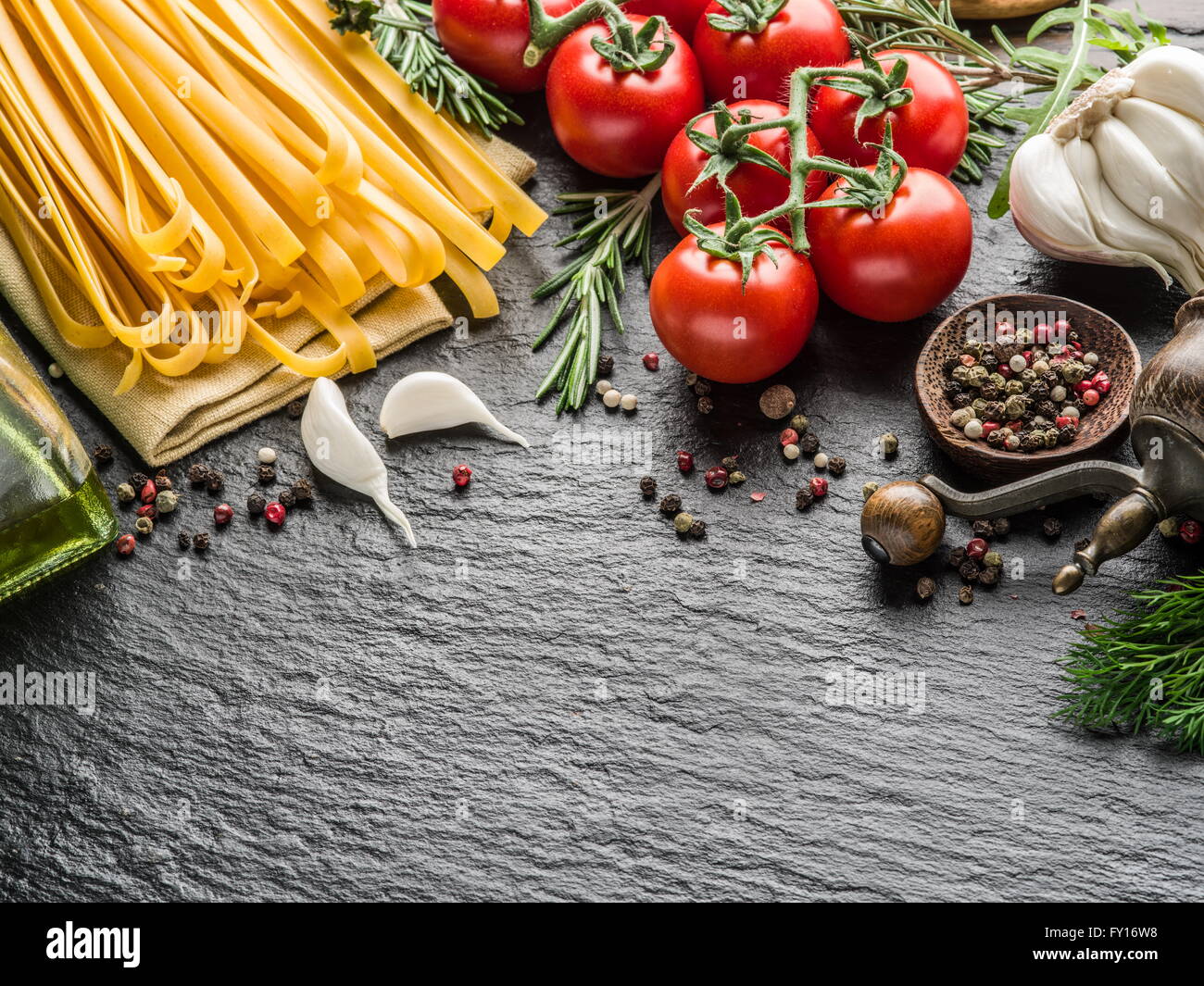 Ingredienti per la pasta. Cherry-pomodori, spaghetti, rosmarino e spezie su una scheda di grafite. Foto Stock