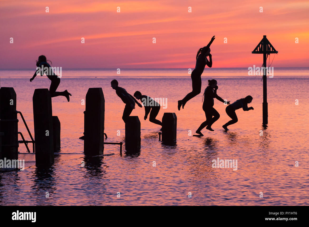 Aberystwyth, Wales, Regno Unito. Il 20 aprile 2016. Alla fine di un glorioso giorno di primavera, un gruppo di giovani continuano tyo godervi il giorno al tramonto le immersioni da un pontile in legno in mare. Credito: Alan Hale/Alamy Live News Foto Stock