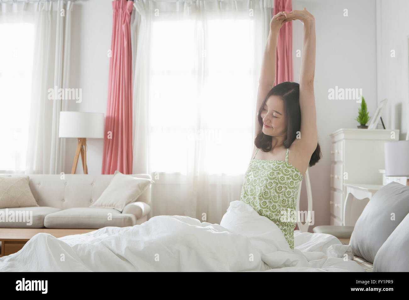Vista laterale della giovane donna sorridente seduta sul letto e bracci di estensione Foto Stock