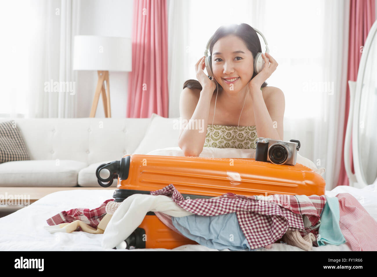 Giovane donna sorridente seduta sul letto ascoltando musica con un carrier Foto Stock
