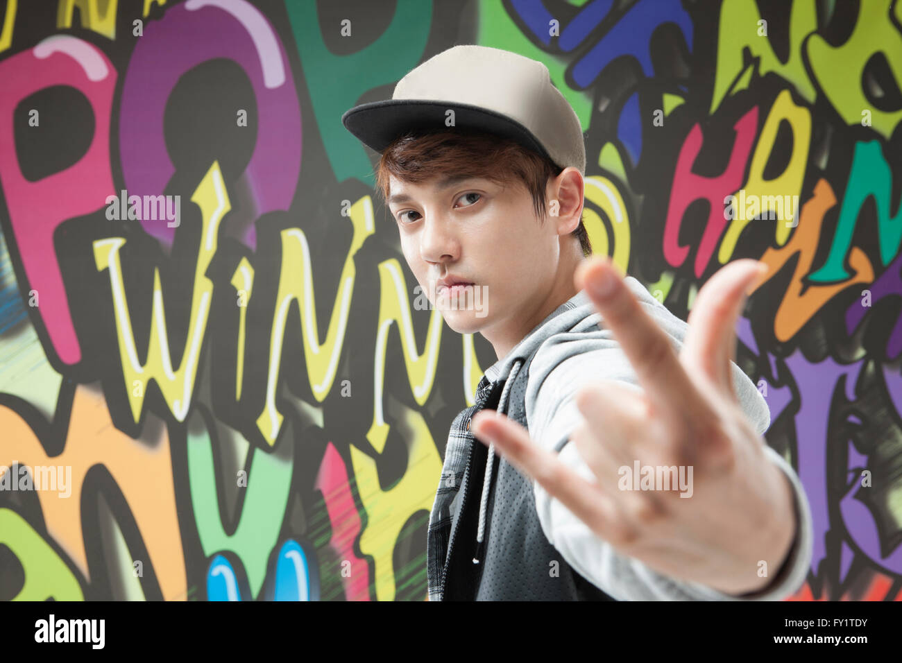 Lato Ritratto di giovane uomo in hip-hop style in posa contro arte dei graffiti Foto Stock