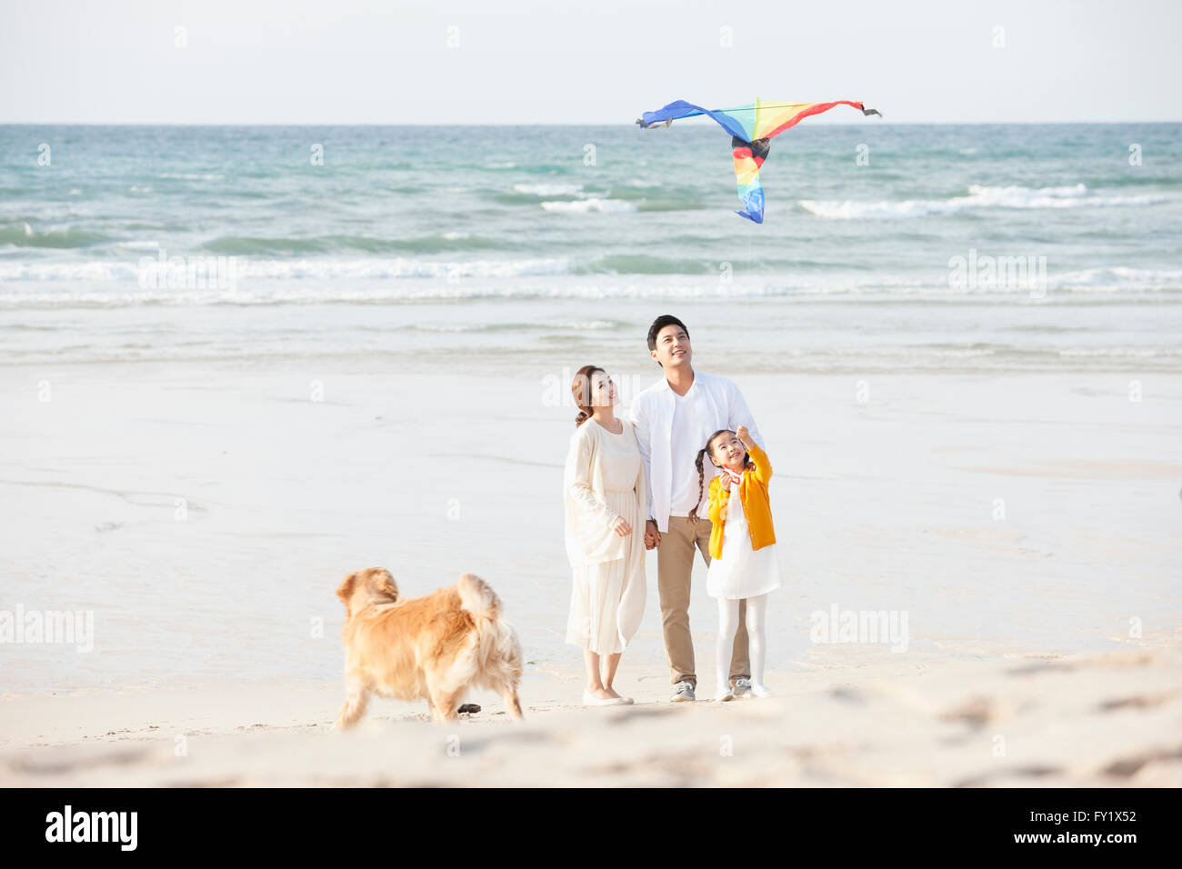 Ragazza volare un aquilone e i suoi genitori in spiaggia con un cane insieme Foto Stock