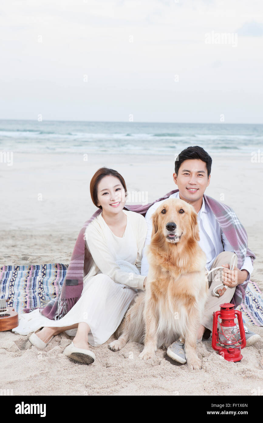 Giovane con un cane seduto su di una spiaggia sabbiosa sia sorridente in avanti Foto Stock