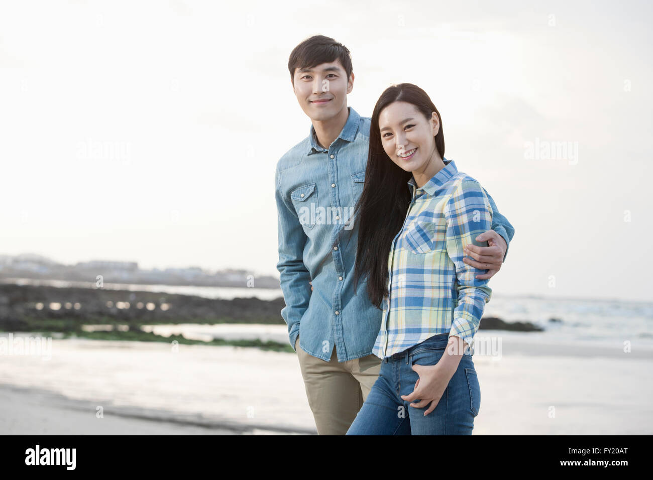 Paio di mettere le loro braccia intorno a ogni altro e sorridente in avanti alla spiaggia Foto Stock