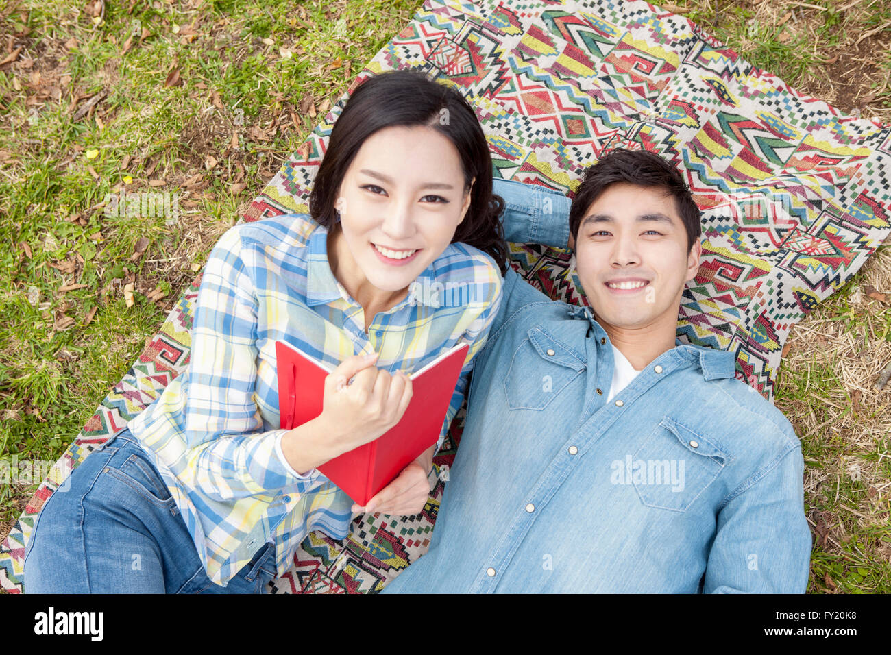 Elevato angolo di una coppia giacendo su erba con un libro sorridente Foto Stock