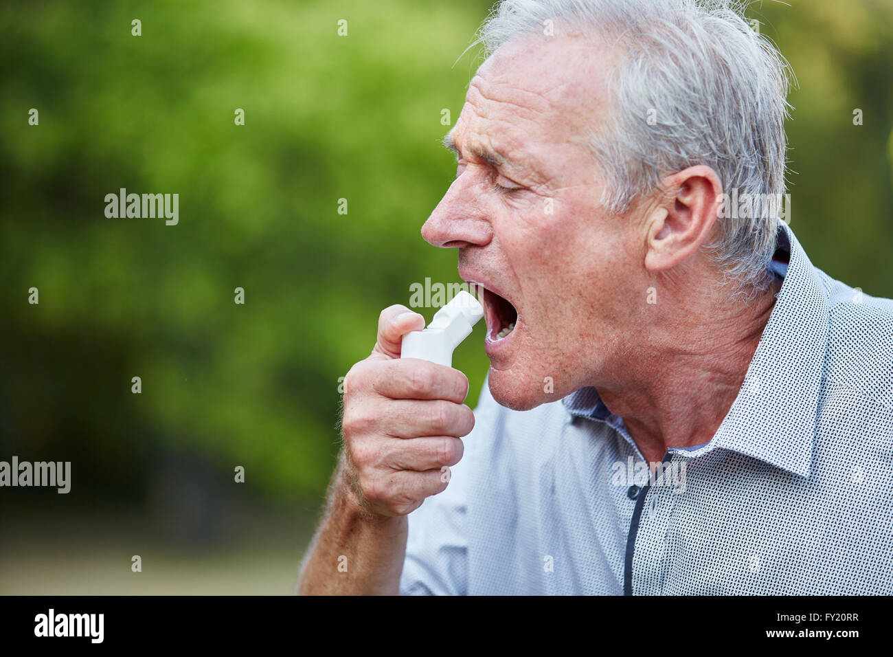Il vecchio uomo utilizzando uno spray come una medicina per la febbre da fieno in natura Foto Stock