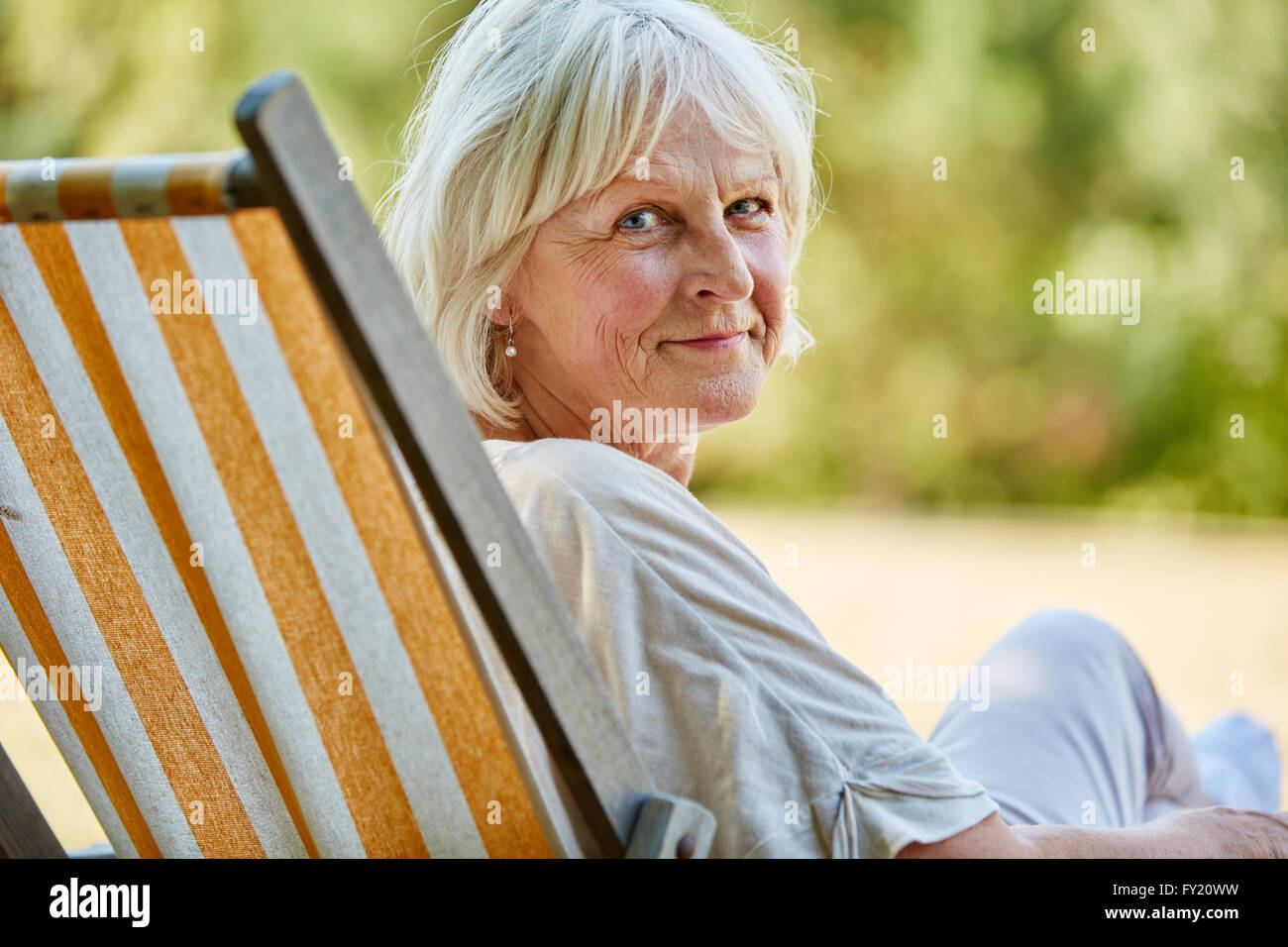 Titolare di pensione o di rendita donna seduta rilassato su una sedia a sdraio in estate Foto Stock