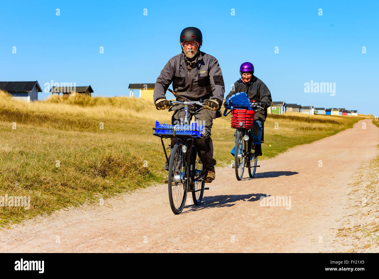 Skanor, Svezia - 11 Aprile 2016: una coppia senior è fuori di equitazione biciclette su strada presso la spiaggia lungo alcune cabine balneari. Entrambi abbiamo Foto Stock