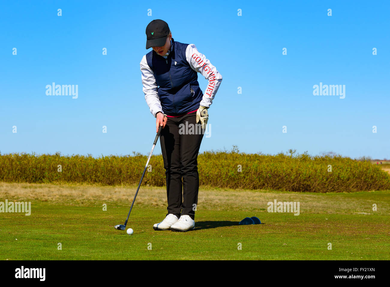 Skanor, Svezia - 11 Aprile 2016: femmina giovane adulto golfista prepara il suo swing sul raccordo a t. Ella è di concentrare e concentrandosi sul suo Foto Stock