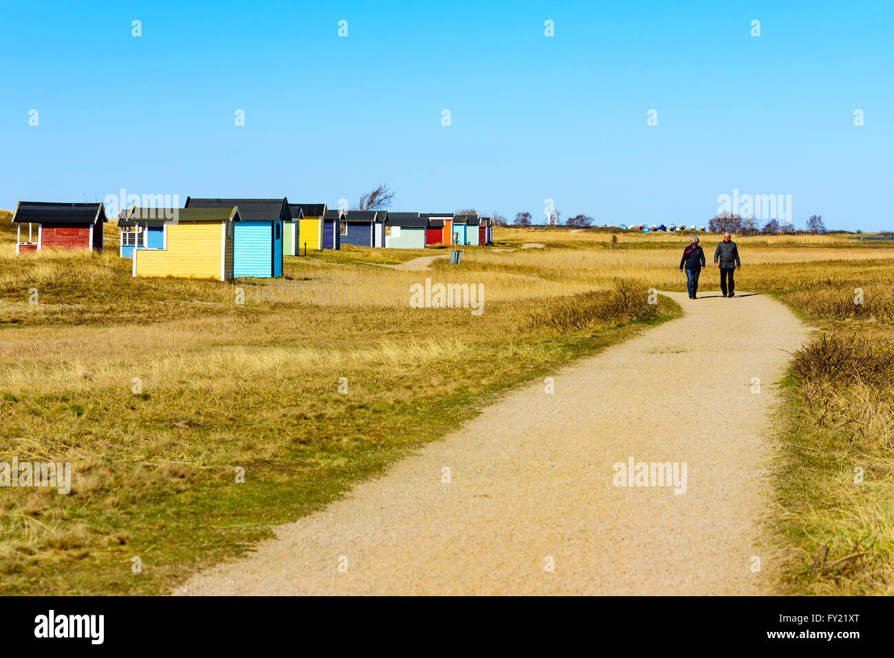 Skanor, Svezia - 11 Aprile 2016: coppia Senior sono fuori per una passeggiata sul sentiero escursionistico dalla spiaggia affiancata da un sacco di cabine balneari Foto Stock