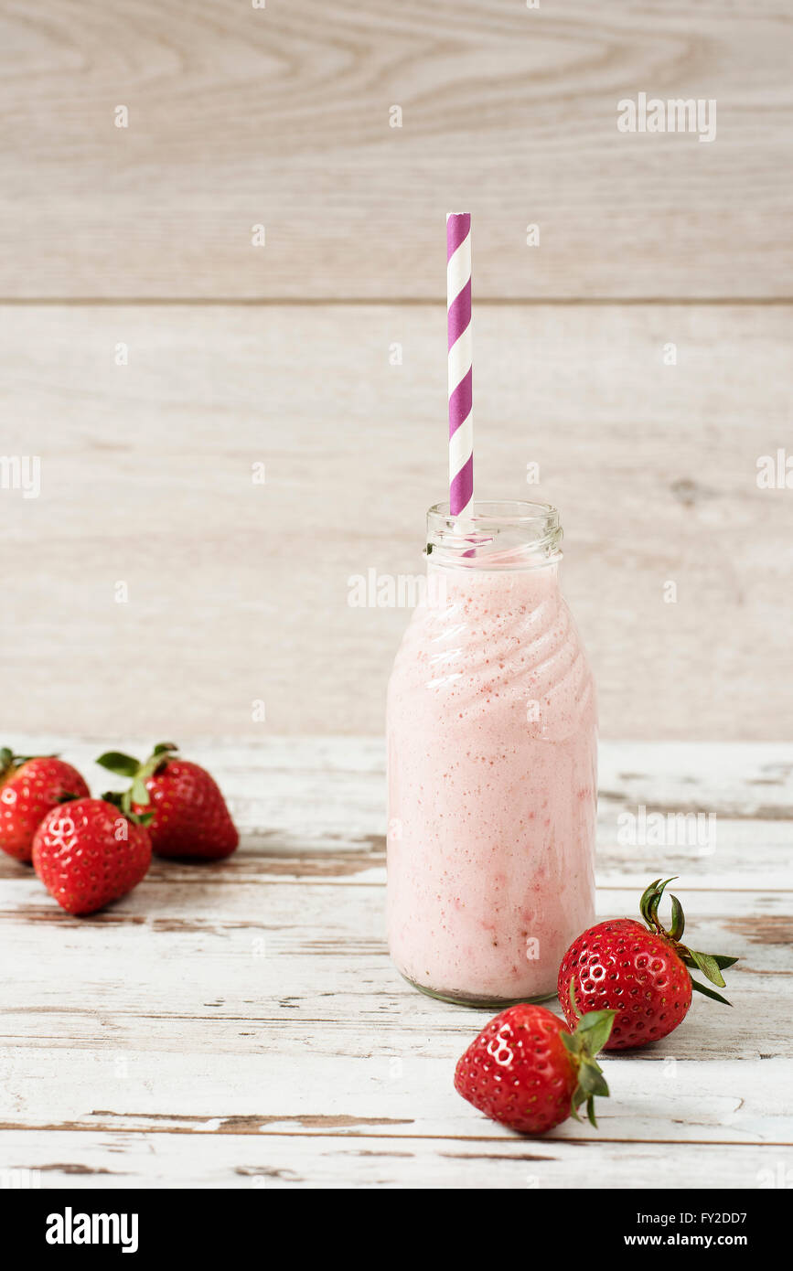 Fragola il latte in bottiglia di vetro con paglia sul vecchio vintage sfondo di legno. Fragole fresche, legno chiaro tavolo. Foto Stock