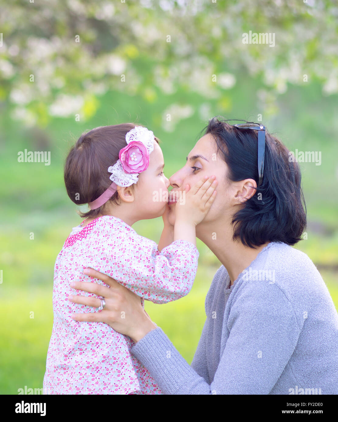 Famiglia i bambini e le persone felici concetto - happy bambina abbracciando e baciando la sua madre su sfondo verde Foto Stock