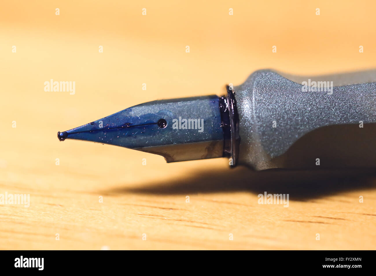 Messa a fuoco ravvicinata sul nasello wet blu inchiostro di penna di fontana sfocata sul tavolo di legno Foto Stock