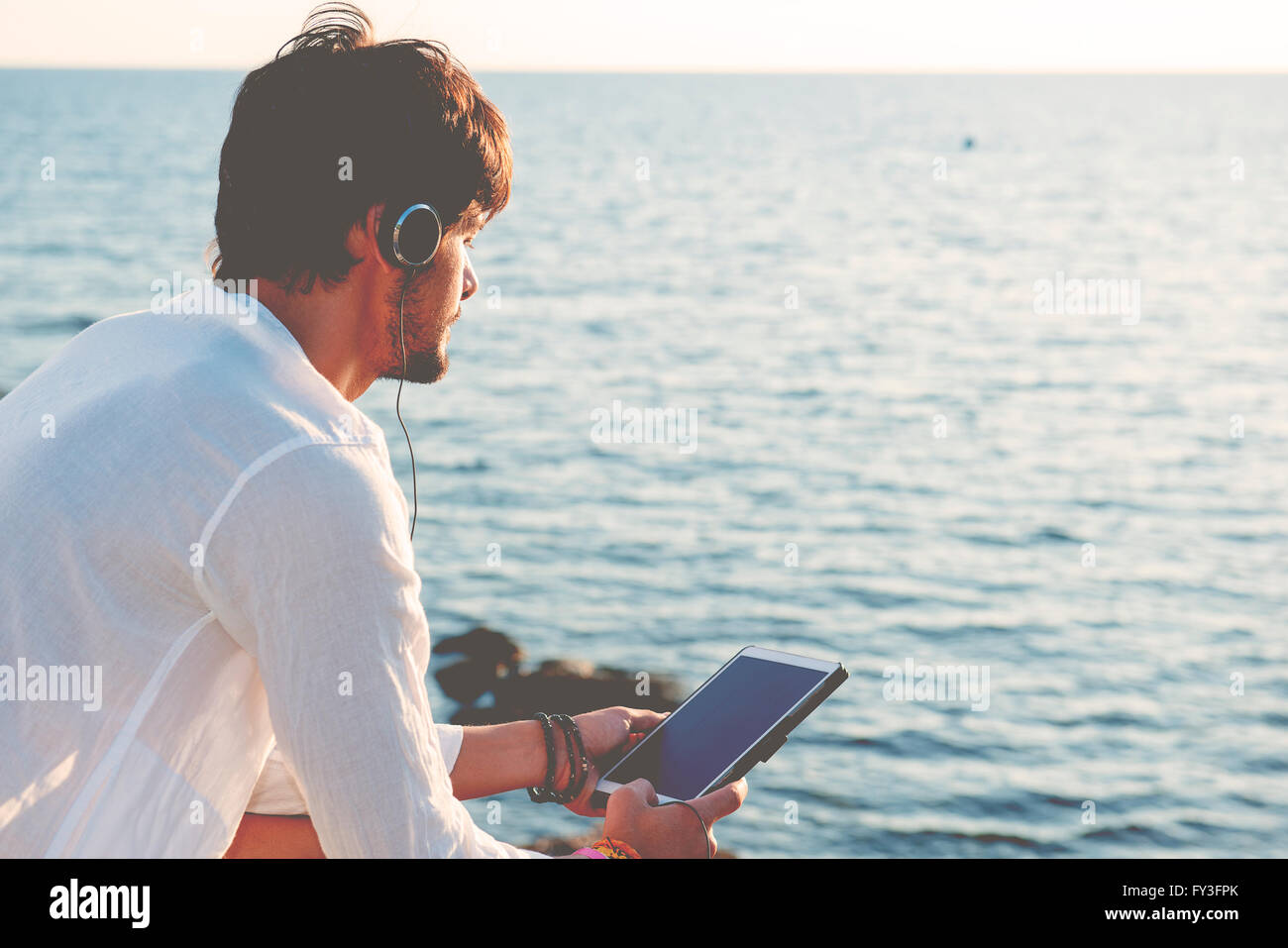 Guy ascoltando musica con le cuffie dalla compressa in una destinazione di vacanze nei pressi di barche Foto Stock