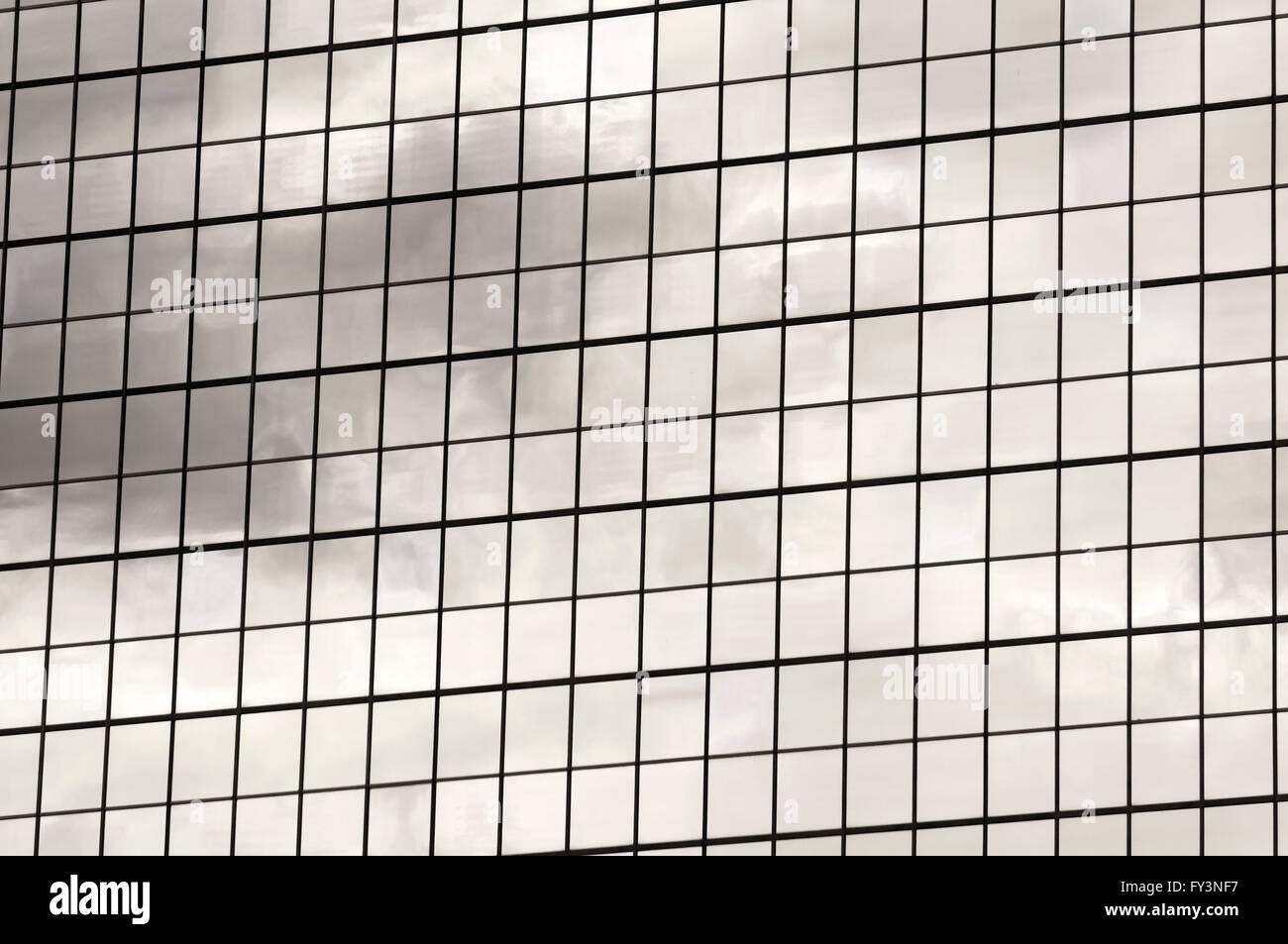Immagine in bianco e nero di un modello a griglia e nubi riflessi sulla facciata di vetro di un edificio per uffici Foto Stock