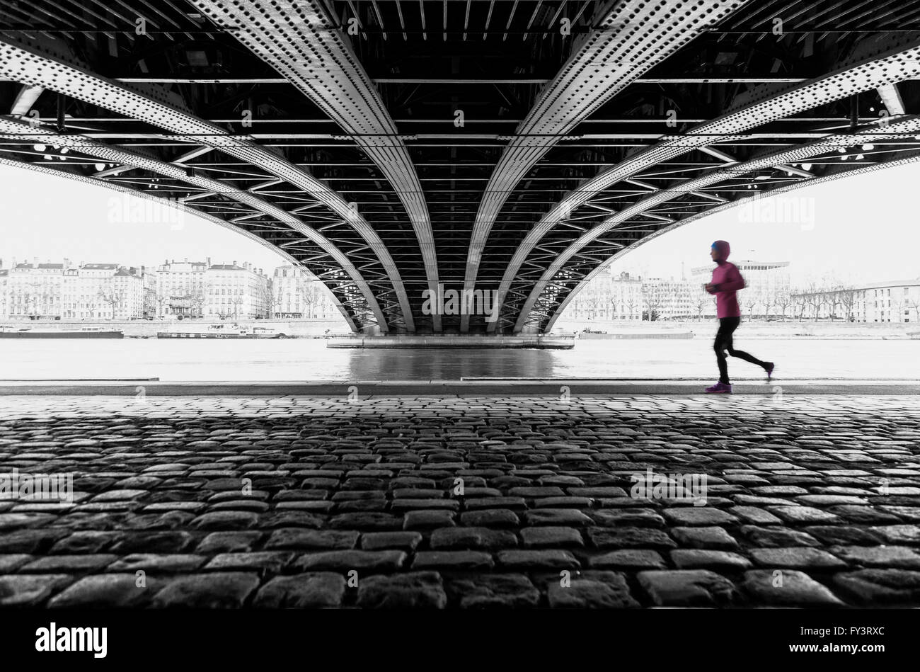 Anonimo atleta femminile in esecuzione sotto un ponte a Lione in una giornata grigia. Con motion blur e poco profonda attenzione. Foto Stock
