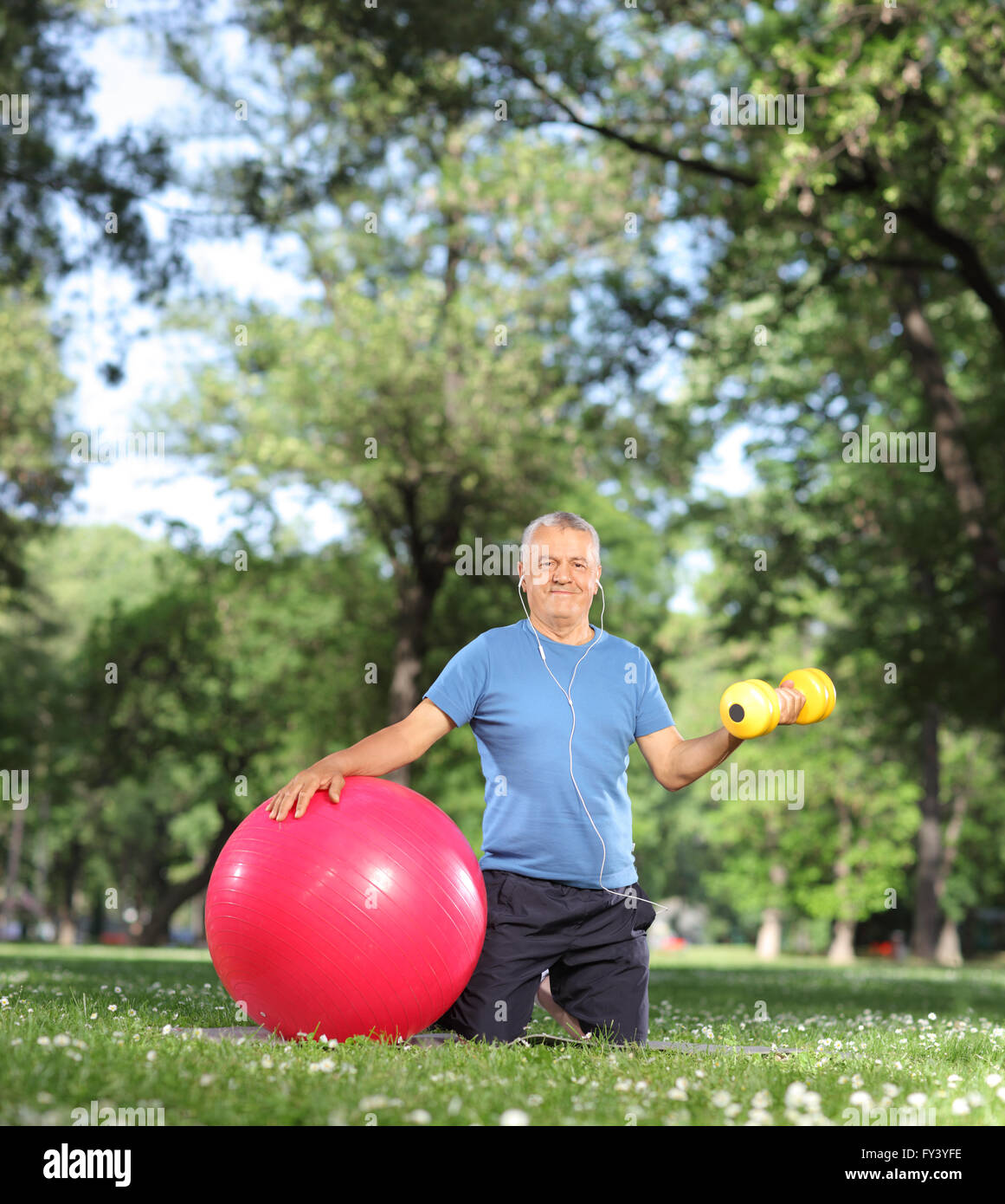 Uomo maturo che esercitano nel parco con un manubrio di colore giallo e una palla fitness shot con inclinazione e spostamento lente Foto Stock