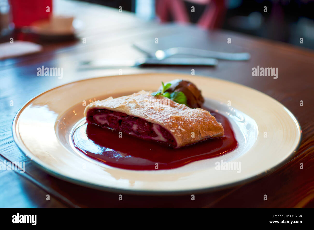 Piastra di strudel di ciliegie a tavola con coltello e forchetta Foto Stock