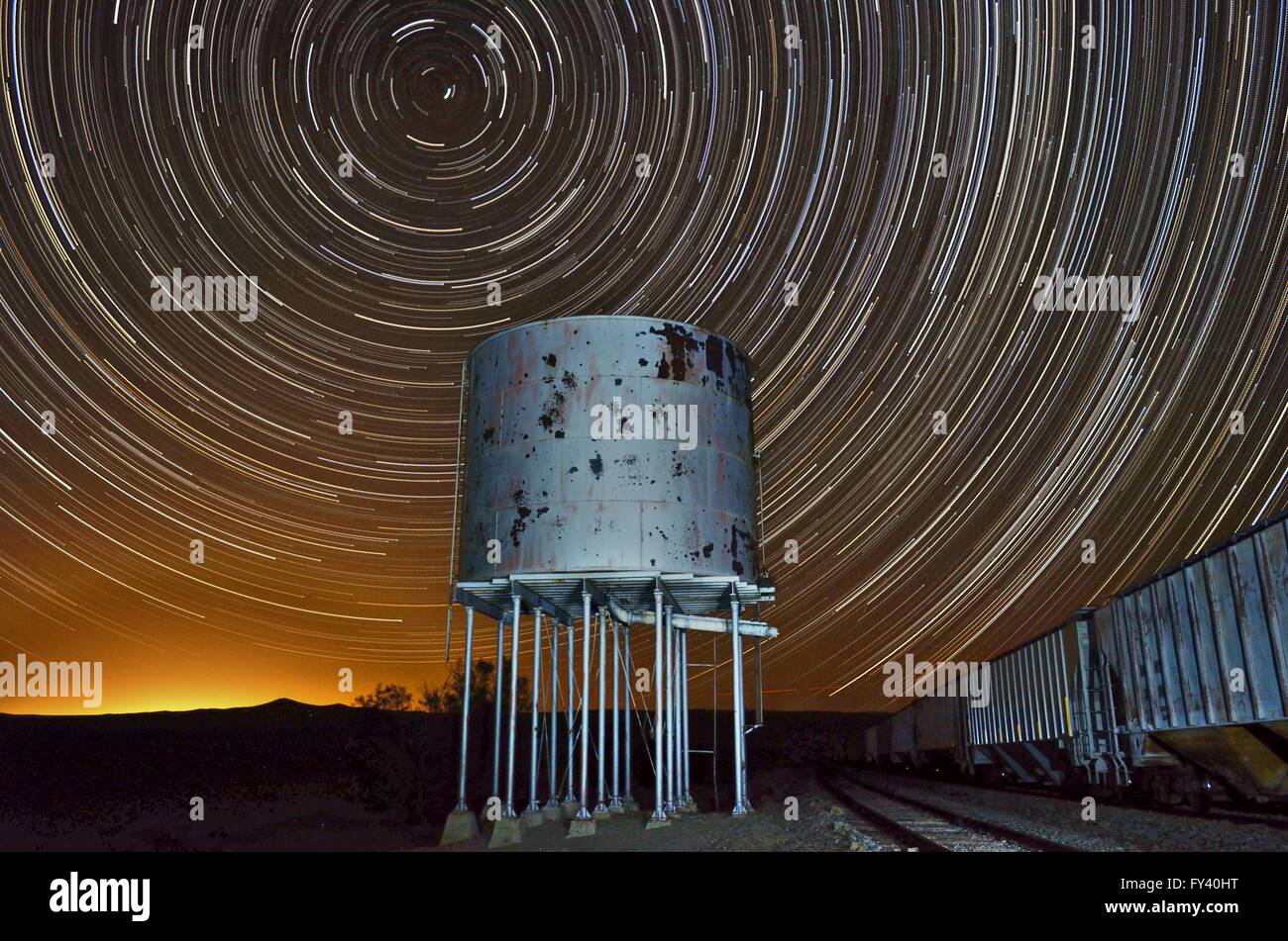 Star trail con la vecchia ferrovia water tower e vagoni ferroviari. Le stelle si formano un modello circolare nel cielo notturno sopra la torre dell'acqua. Foto Stock