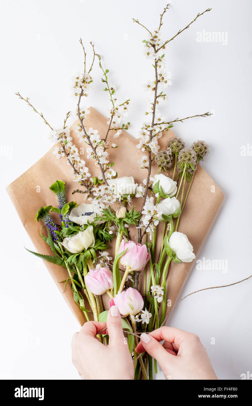 Mani Imballare fiori: rosa tulipani, anemoni bianchi, bianco renoncules e prugna Fiore di ramo di albero giacente sulla carta di avvolgimento Foto Stock