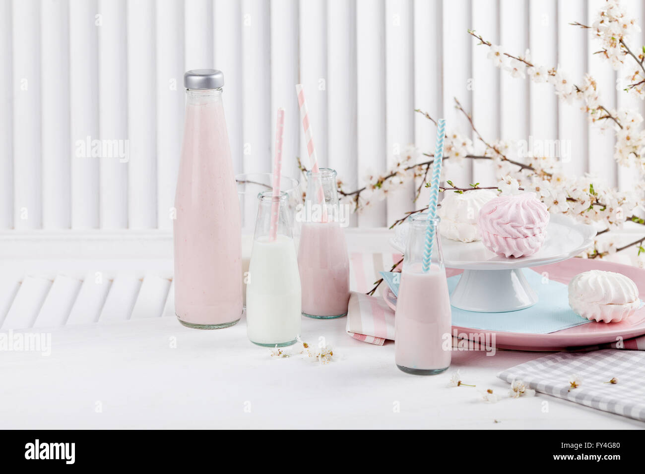 Quattro bottiglie di frappè, tre con cannucce e piastre con rosa e bianco meringhe e panno sul bianco otturatore in legno Foto Stock