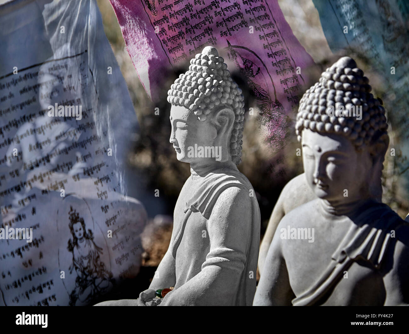 Figure buddista di cemento seduti in meditazione con la preghiera e le offerte di bandiere di preghiera Foto Stock