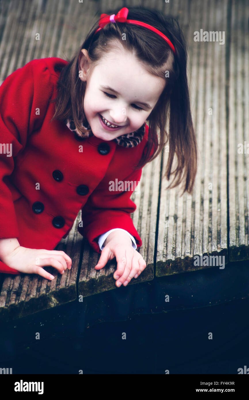 Una piccola ragazza seduta sul legno da soli e sorriso Foto Stock
