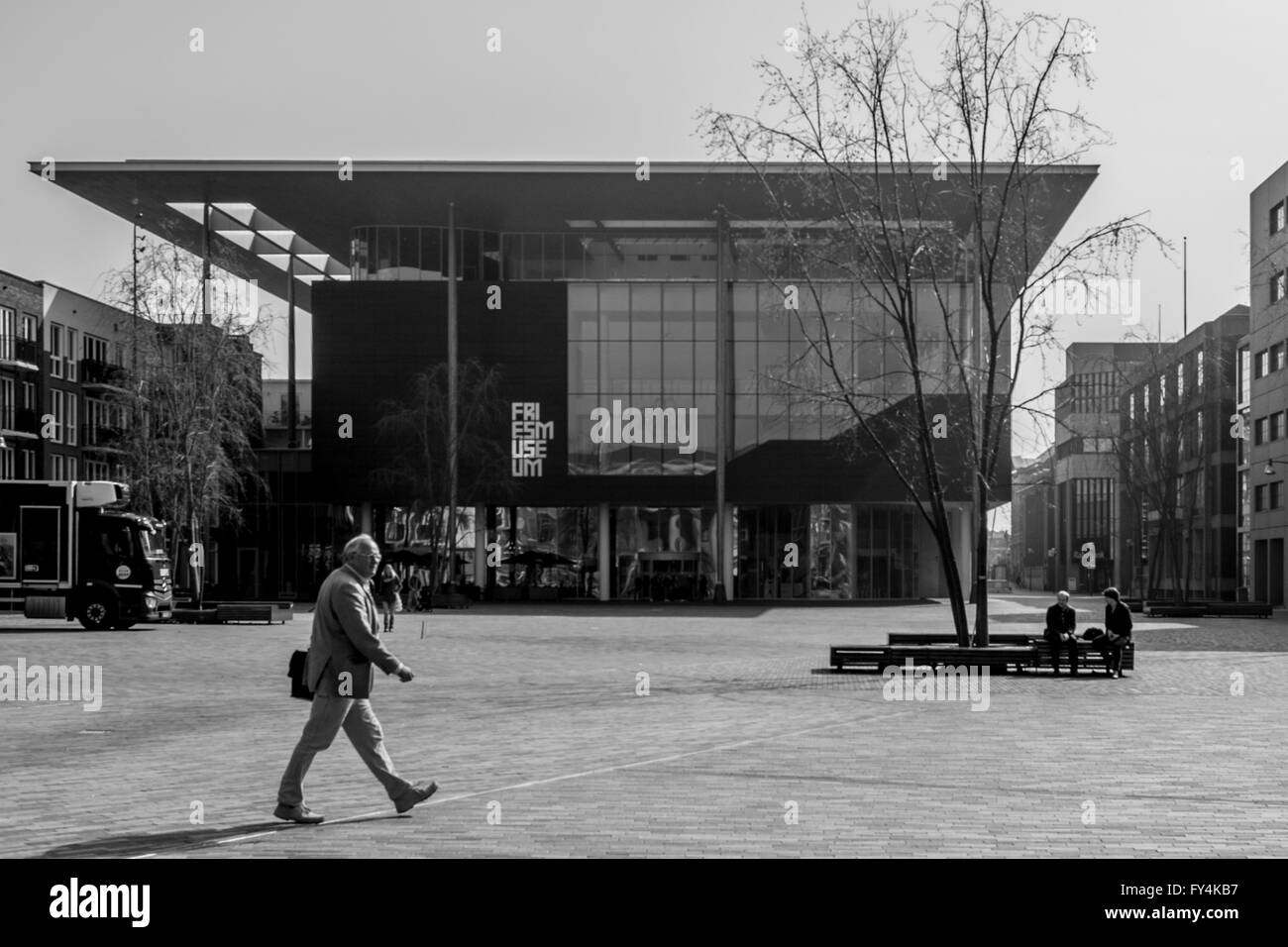 Un uomo cammina passeggiate attraverso la piazza principale di Leuwarden in questa fotografia in bianco e nero. Fretta architettura moderna in Olanda. Foto Stock