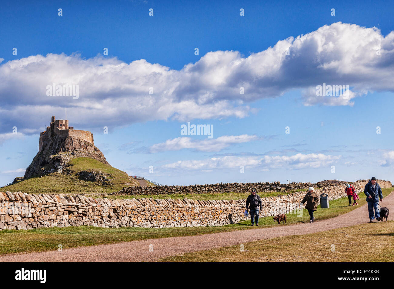 La gente a piedi giù per la pista da Lindisfarne Castle, Isola Santa, Northumberland, Regno Unito, su una luminosa giornata di primavera. Foto Stock